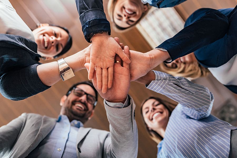 Insurance Quote - Group of Smiling Employees at the Office Joining Their Hands Together
