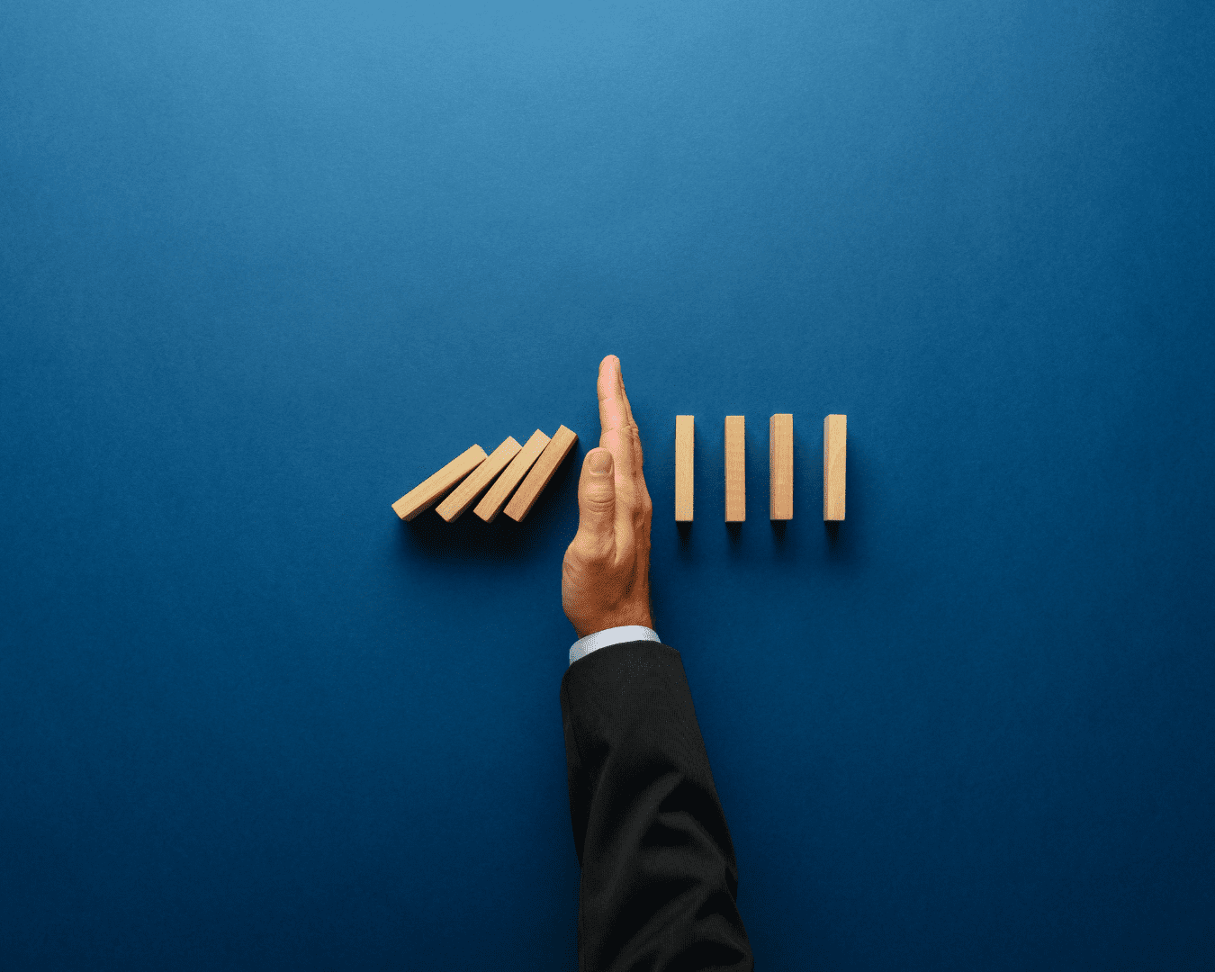 Hand stopping dominoes from continuing to fall. Risk management concept.